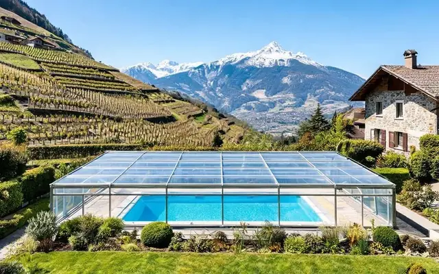 Abri de piscine télescopique bas au-dessus d'un bassin privé dans un jardin de villa à Sion en Valais, montagnes alpines en arrière-plan